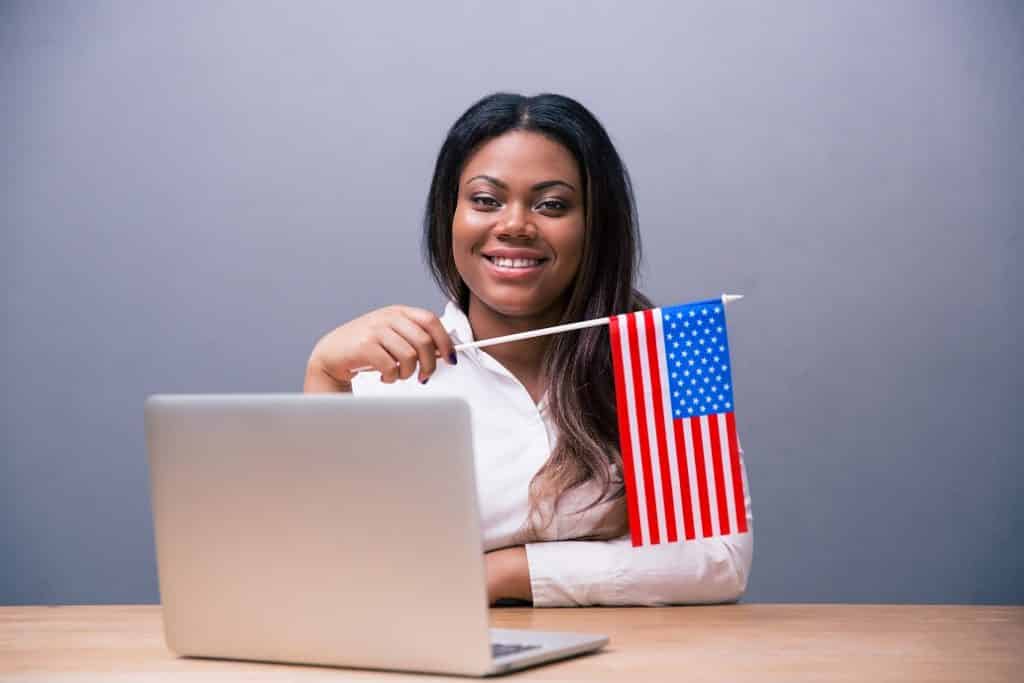 בחורה עם שיער שחור יושבת מול מחשב נייד מחזיקה דגל אמריקה