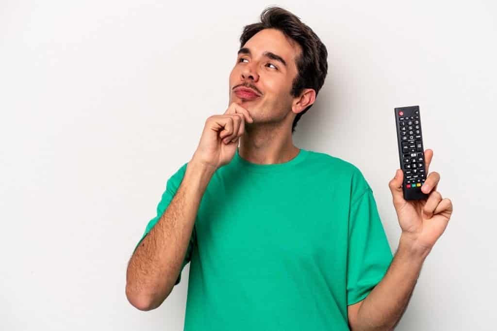 בחור בחולצה ירוקה מחזיק שלט של טלוויזיה יד על הסנטר חושב