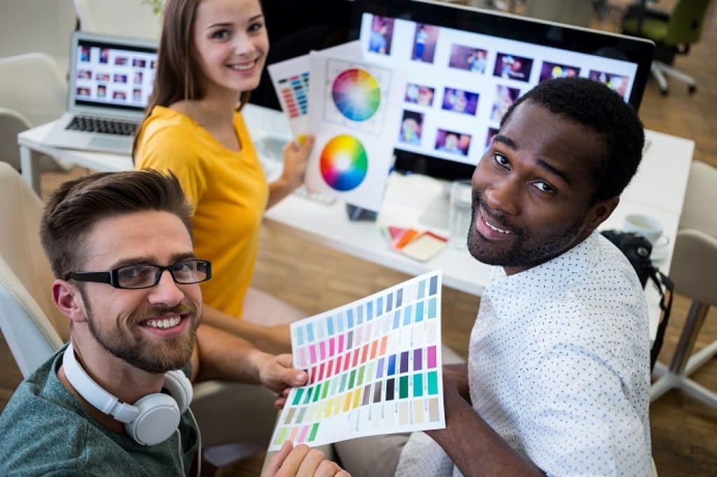 שלושה אנשים יושבים ליד מחשב מחייכים ומחזיקים דפים עם מפת צבעים