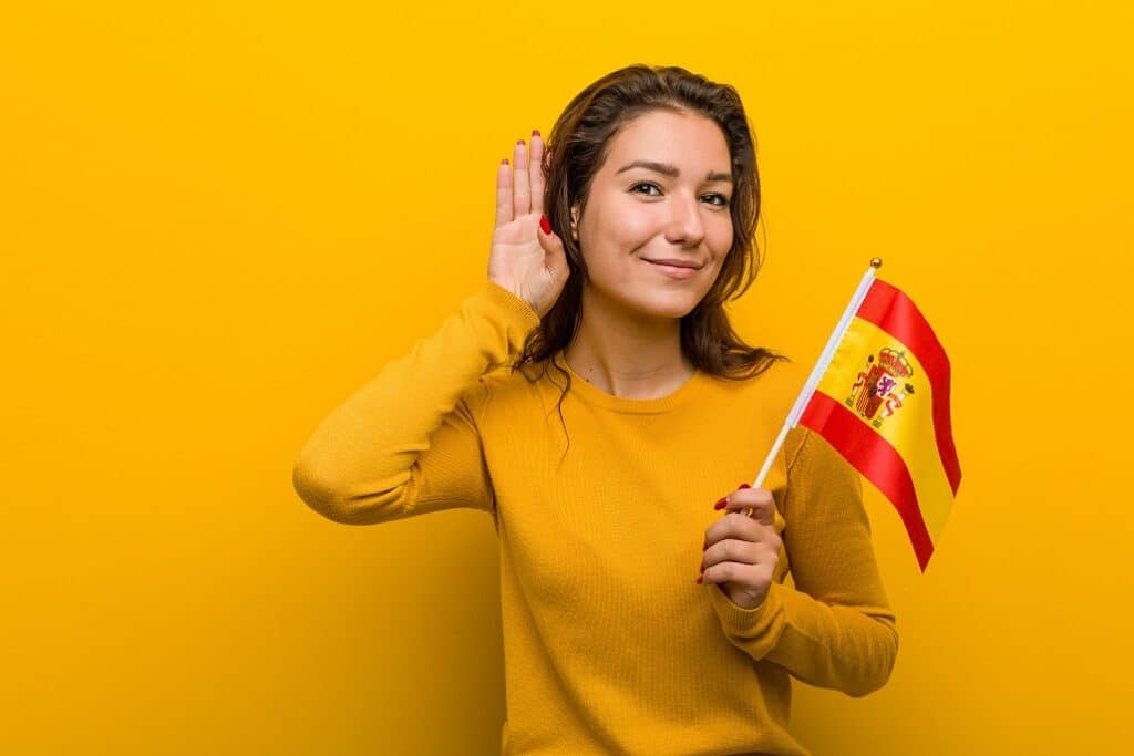 בחורה בחולצה צהובה מחזיקה דגל ספרד ומחייכת רקע צהוב