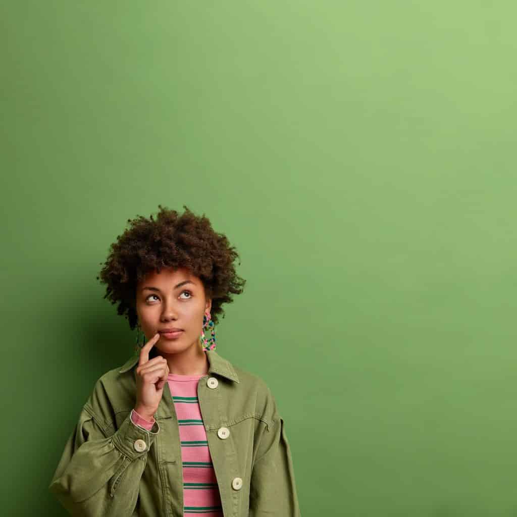 בחורה בחולצת פסים וגקט ירוק יד על הסנטר חושבת רקע ירוק