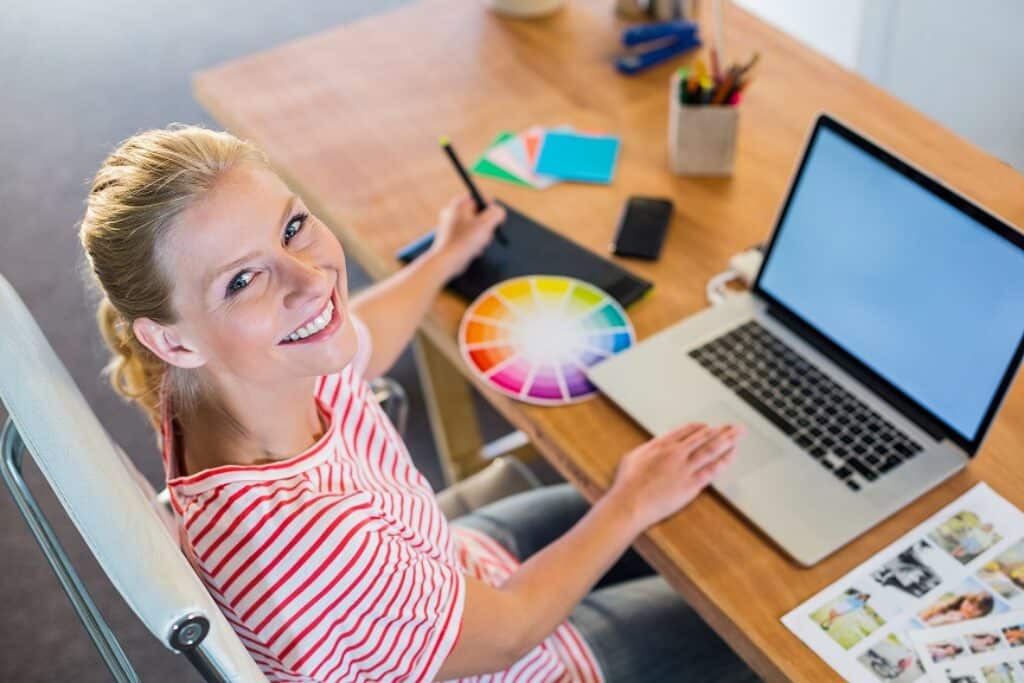בחורה בלונדינית יושבת ליד מחשב מביטה למעלה ומחייכת מעצבת גרפית
