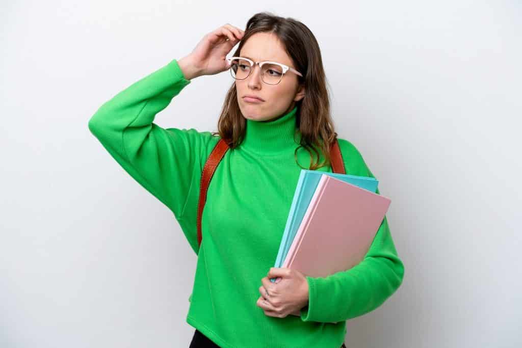 בחורה בסוודר ירוק ותיק גב מחזיקה מחברות חושבת רקע לבן