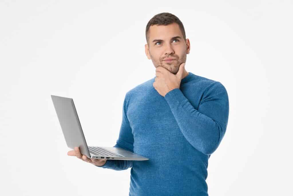 בחור בחולצה כחולה מחזיק מחשב נייד וחושב יד על הסנטר רקע לבן