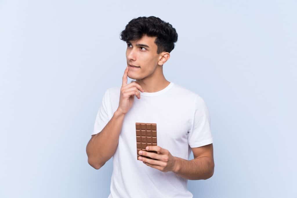 בחור בחולצה לבנה מחזיק טבלת שוקולד וחושב רקע לבן