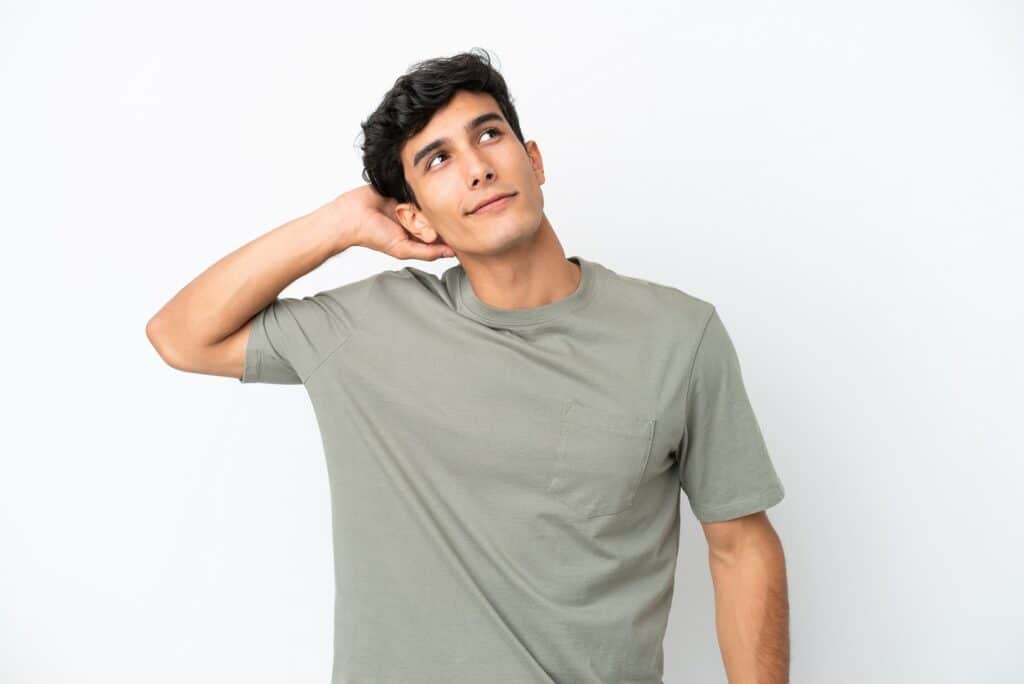 בחור צעיר בחולצת טישרט ירוקה חושב יד על הראש רקע לבן