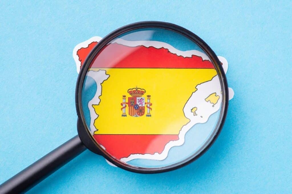 זכוכית מגדלת מונחת על דגל ספרד על רקע תכלת