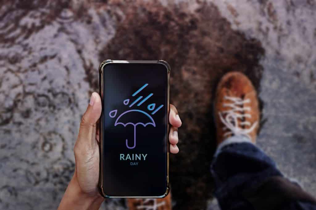 יד מחזיקה סמארטפון עם אפליקציית מזג האוויר ורגל עם נעל הליכה ברקע