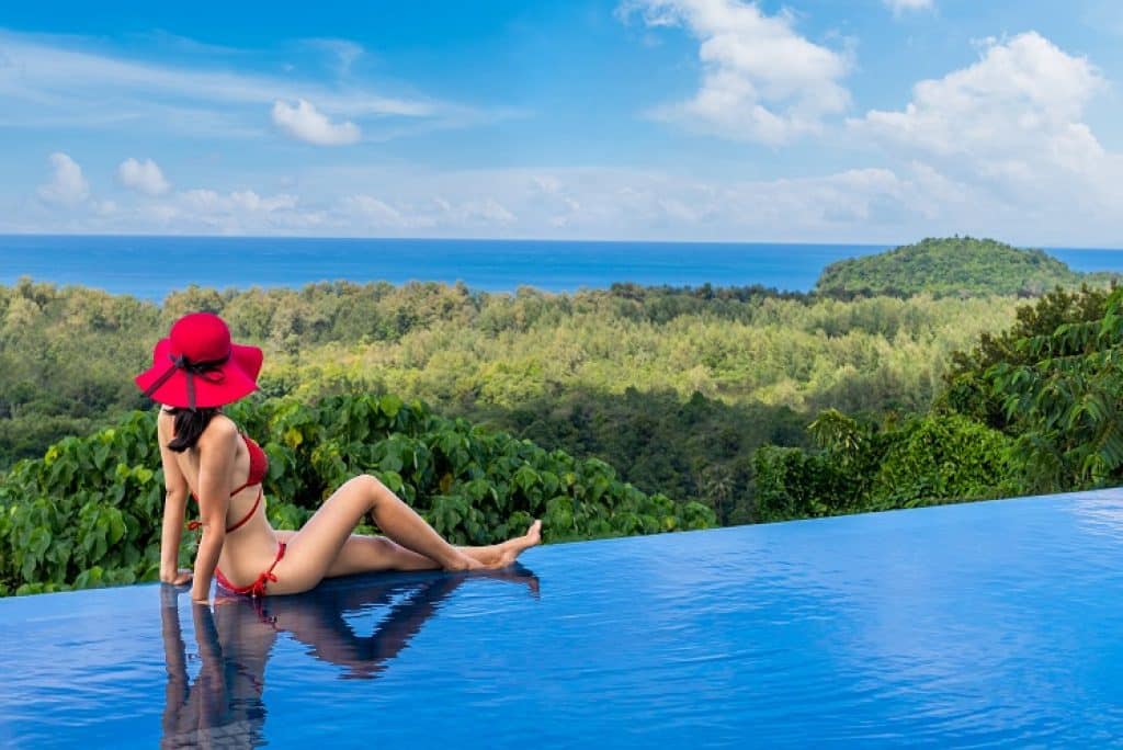 בחורה בבגד ים אדום יושבת על שפת הבריכה מביטה בנוף בתאילנד