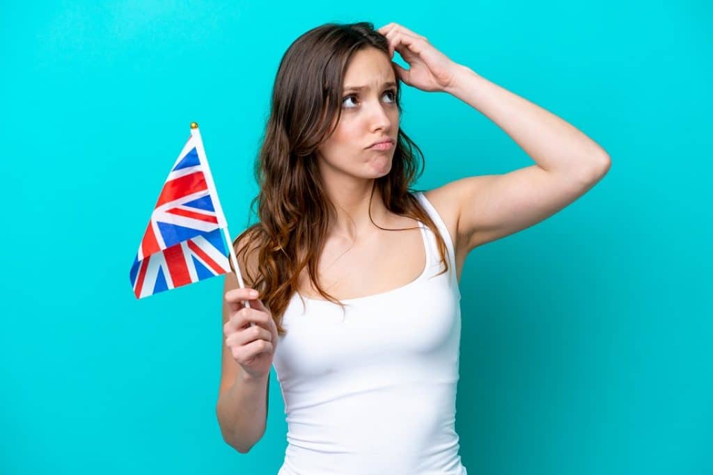 בחורה בגופיה לבנה מחזיקה דגל של אנגליה יד על המצח חושבת