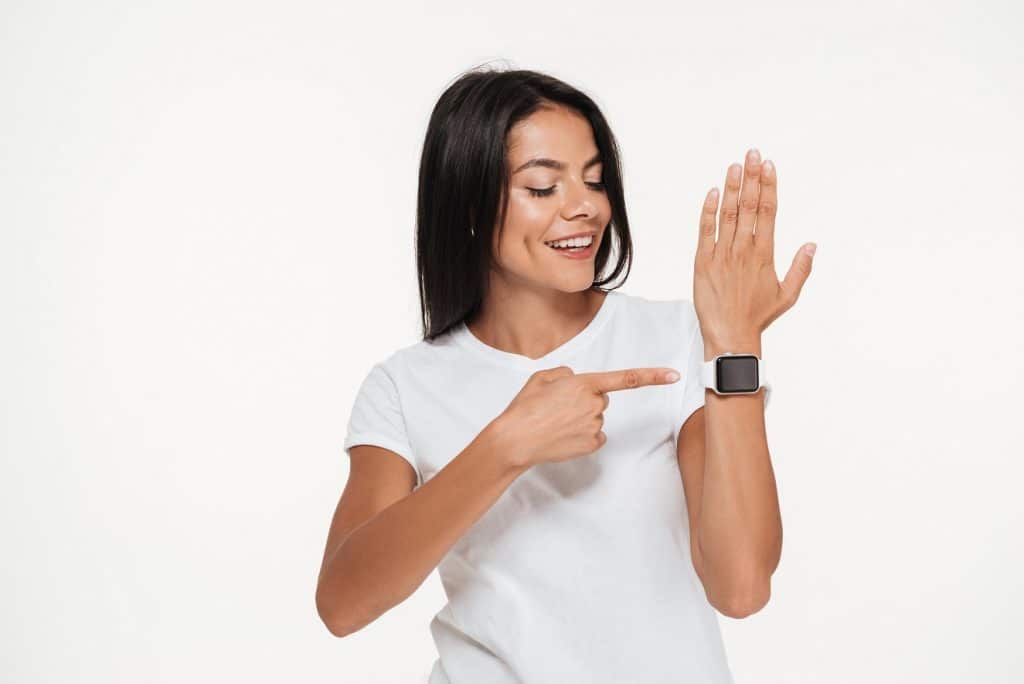 בחורה מחייכת בחולצה לבנה מצביעה על שעון חכם רקע לבן
