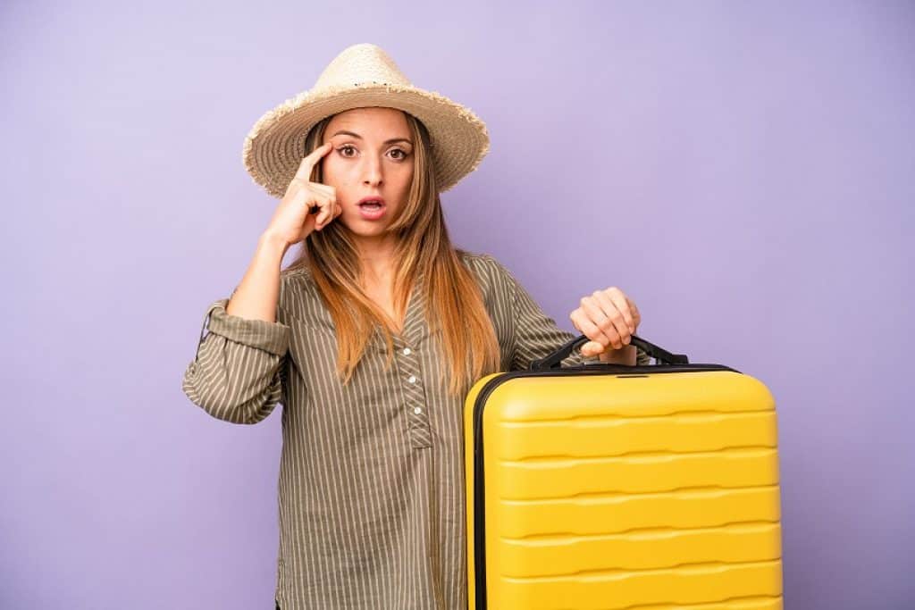 בחורה עם כובע קש מחזיקה מזוודה צהובה וחושבת על חופשה רקע סגול