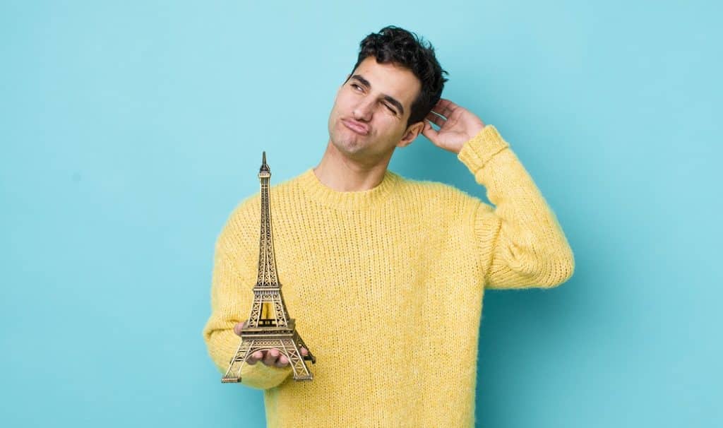 בחור בסוודר צהוב מחזיק דגם של מגדל אייפל בפריז וחושב רקע תכלת