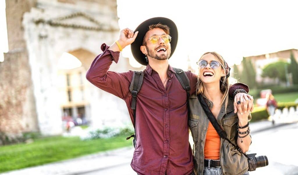 בחור ובחורה תיירים עם משקפי שמש ומצלמה שמחים ומטיילים ברומא
