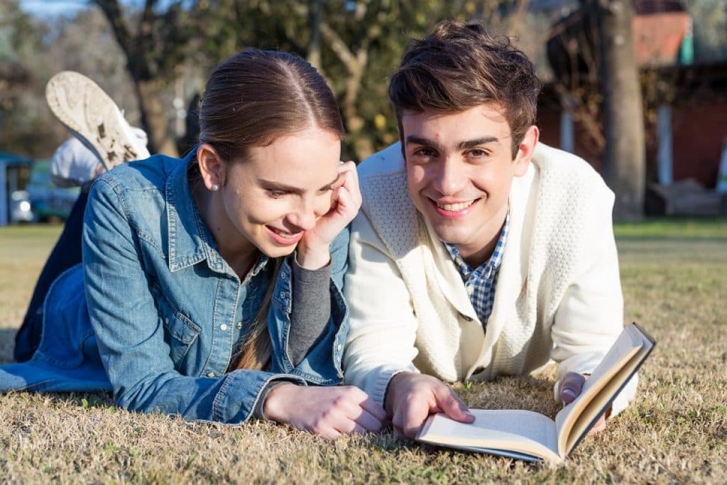 נער ונערה שוכבים על הדשא בחוץ קוראים ספר ומחייכים