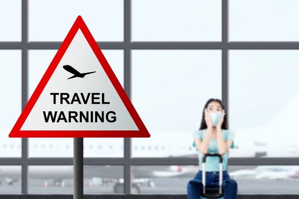 שלט אזהרה עם המילים אזהרת נסיעה וברקע אישה יושבת עם מזוודה