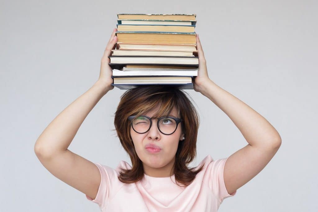 בחורה אסיאתית עם משקפי קריאה מחזיקה ערמת ספרים על הראש