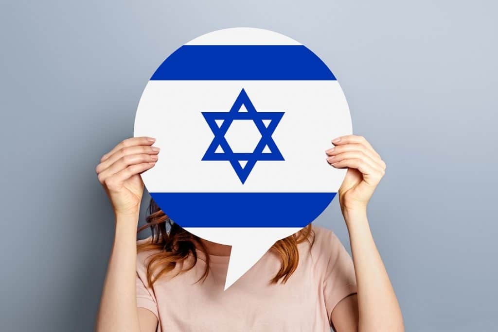 בחורה בחולצה ורודה מחזיקה בלון דיבור שבתוכו דגל ישראל רקע אפור