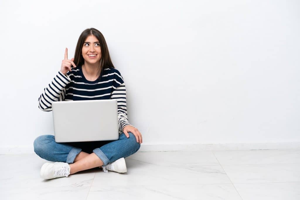 בחורה בחולצת פסים מחייכת יושבת על הרצפה עם מחשב נייד על הרגליים