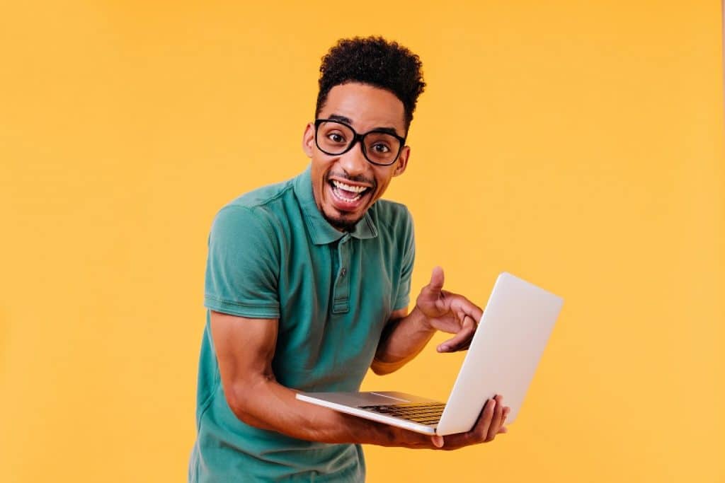 בחור בחולצה כחולה ומשקפיים מחזיק מחשב נייד מחייך רקע כתום 