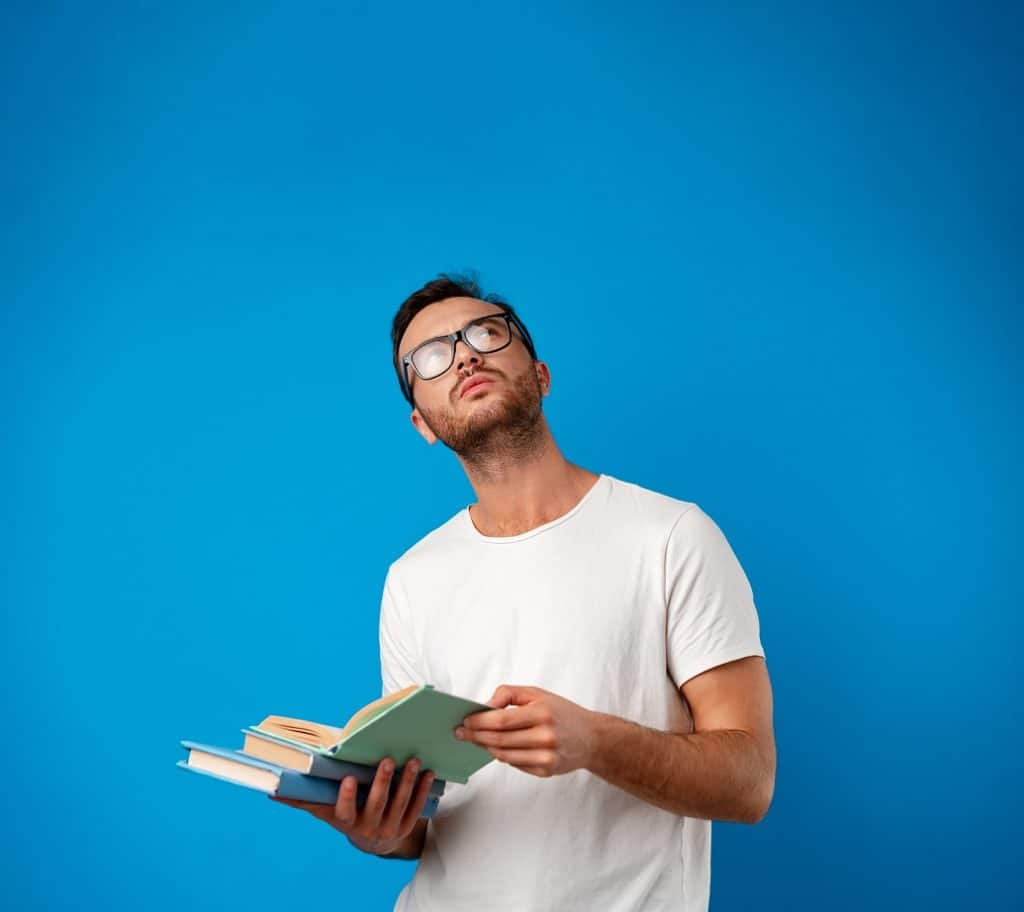בחור בחולצה לבנה עם משקפיים מחזיק ספר מסתכל למעלה וחושב