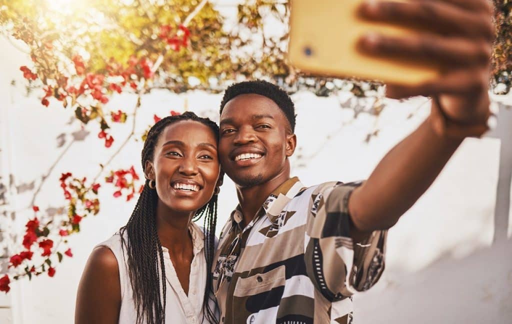 בחור ובחורה אפריקאים מחייכים מחזיקים סמארטפון זול ועושים סלפי