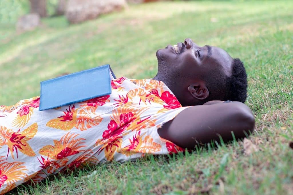 בחור שוכב על הדשא עוצם עיניים ומחייך עם ספר כחול מונח על החזה