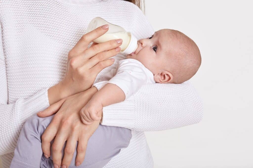 ידיים מחזיקות תינוק ששותה חלב מבקבוק רקע לבן