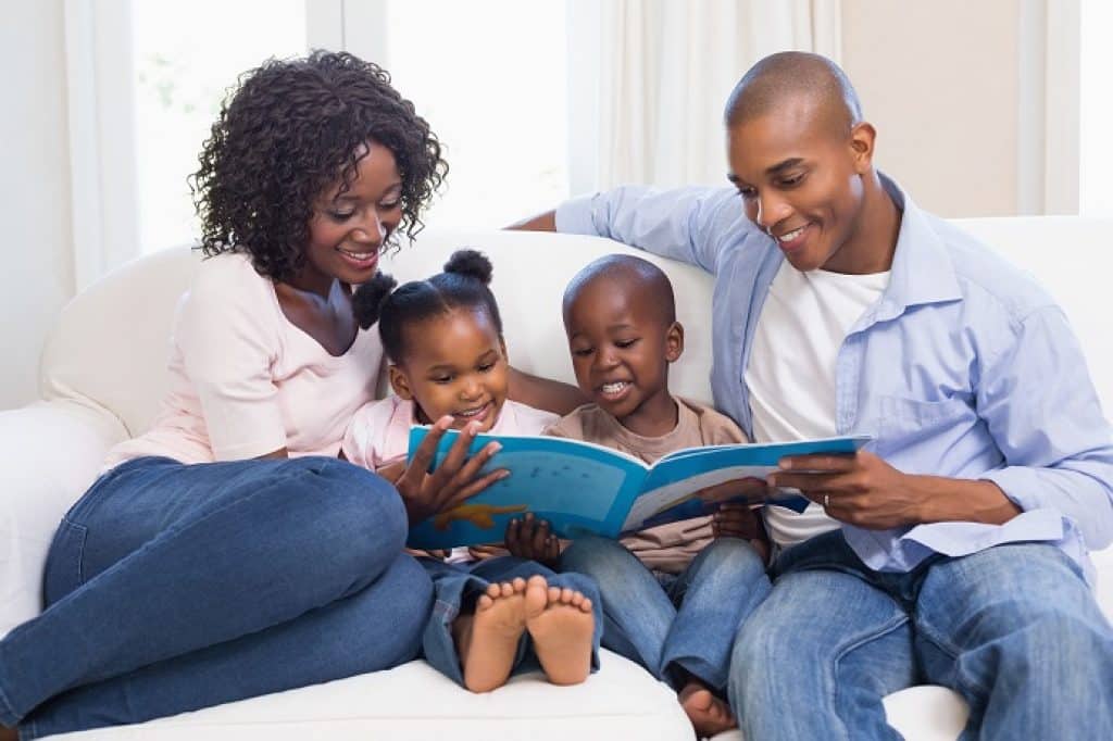 משפחה הורים וילדים יושבים על ספה וקוראים ספר ביחד שמחים