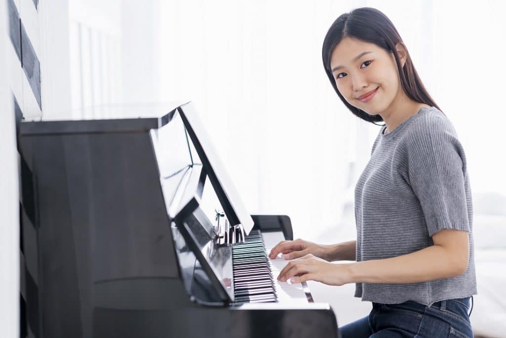 בחורה אסיאתית בחולצה אפורה מחייכת ומנגנת בפסנתר חשמלי