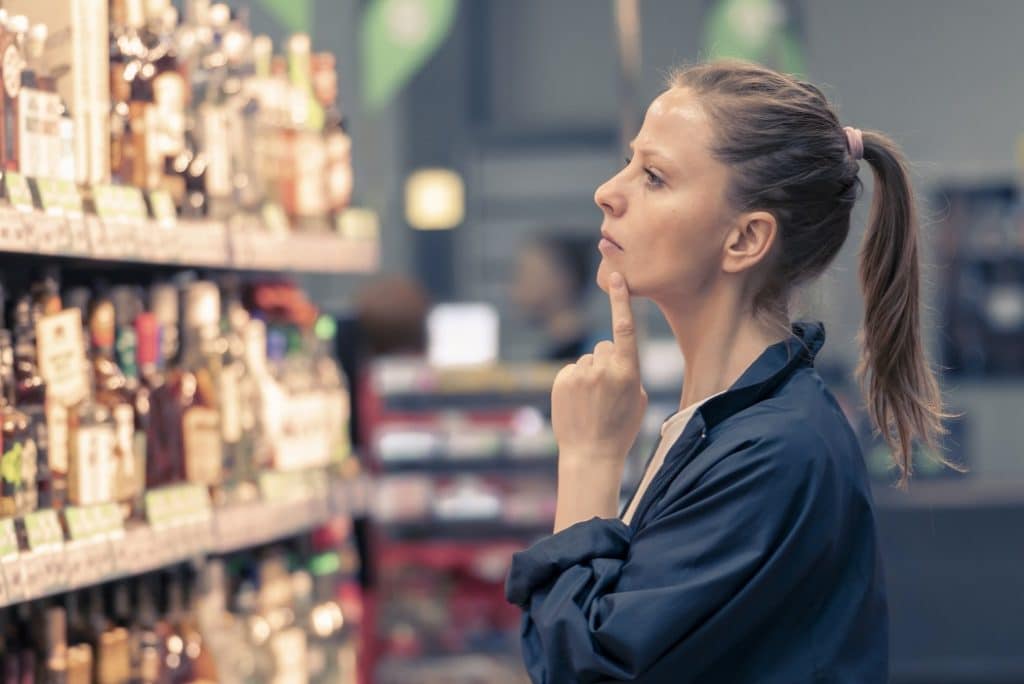 בחורה בלונדינית בחנות למשקאות אלכוהולים מסתכלת על המדף בוחרת קוניאק