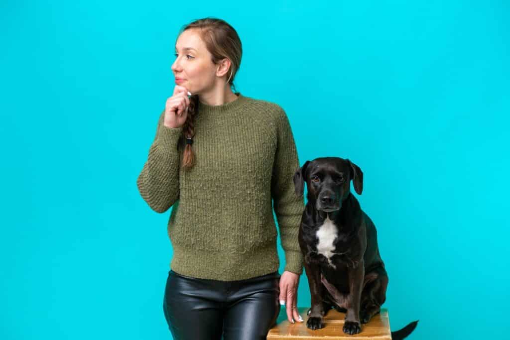 בחורה בסוודר ירוק חושבת ולידה כלב שחור רקע תכלת