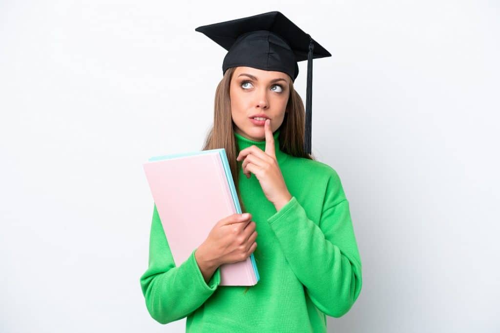 בחורה בסוודר ירוק עם כובע סטודנט מחזיקה מחברות וחושבת רקע לבן