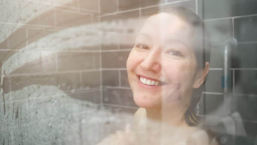בחורה מחייכת דרך חלון מקלחת מכוסה באדים חמים