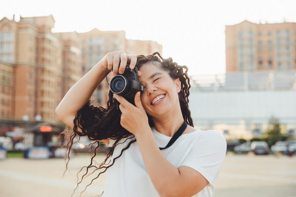 בחורה מחייכת ומאושרת בחולצה לבנה מחזיקה מצלמה על העין