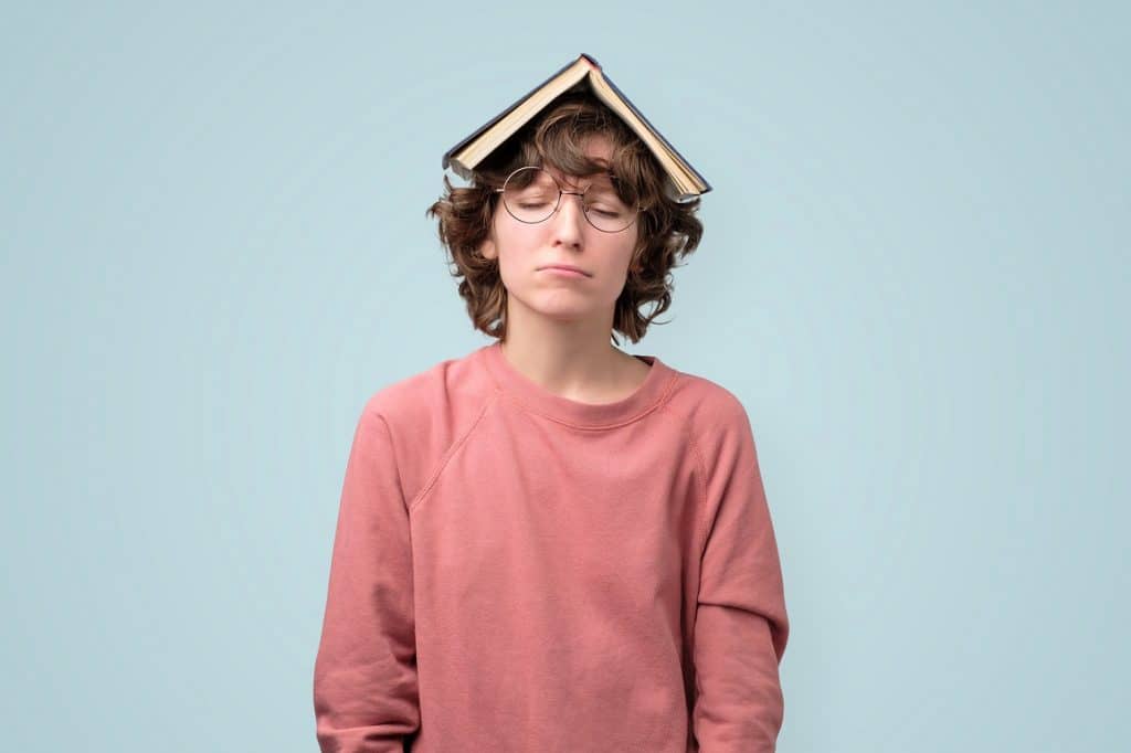 בחורה צעירה בסוודר ורוד עם משקפיים וספר פתוח על הראש רקע תכלת