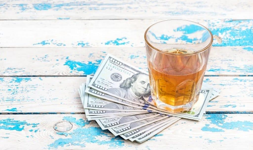 כוס עם וויסקי מונחת על שולחן עץ עם שטרות כסף מתחת