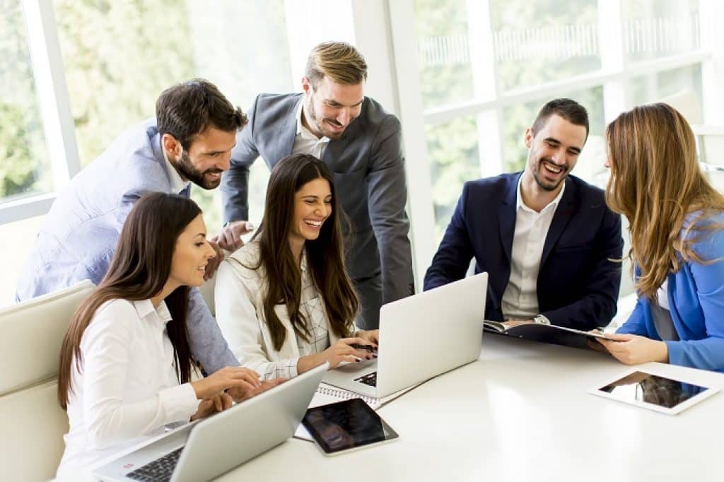 קבוצת יועצים עסקיים מחייכים ושמחים מסתכלים במחשב נייד במשרד