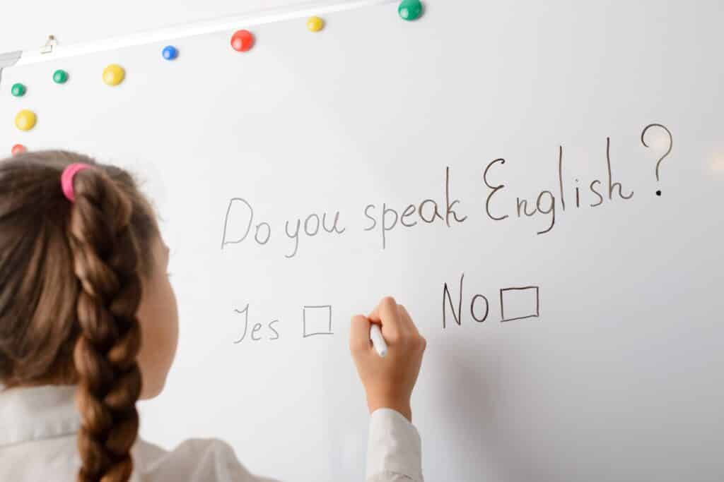 ילדה כותבת על לוח מחיק עם המילים האם אתה יודע אנגלית