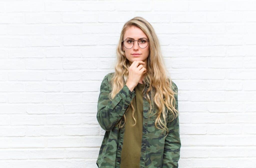 בחורה בלונדינית לבושה בבגדים צבאיים עם משקפיים חושבת רקע לבן