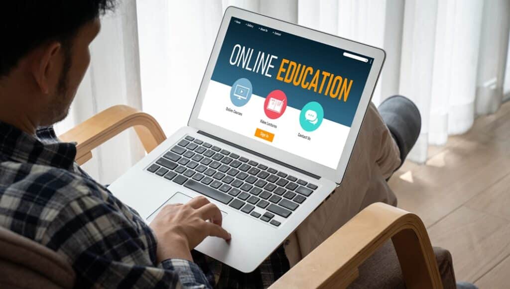 איש יושב מול מחשב נייד שעליו כתוב למידה באנטרנט קורסים אונליין