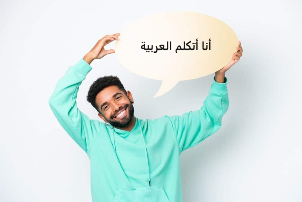 בחור מחייך בסוודר תכלת מחזיק שלט עליו כתוב אני מדבר בערבית