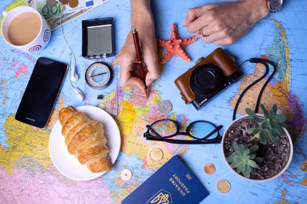 ידיים מחזיקות עט מעל מפת עולם עם מצלמה משקפיים דרכון טלפון קפה ומאפה