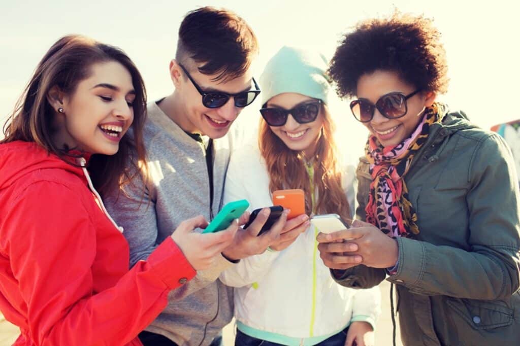 קבוצת חברים במשקפי שעומדים יחד מחזיקים סמארטפונים ומחייכים בטיול משותף