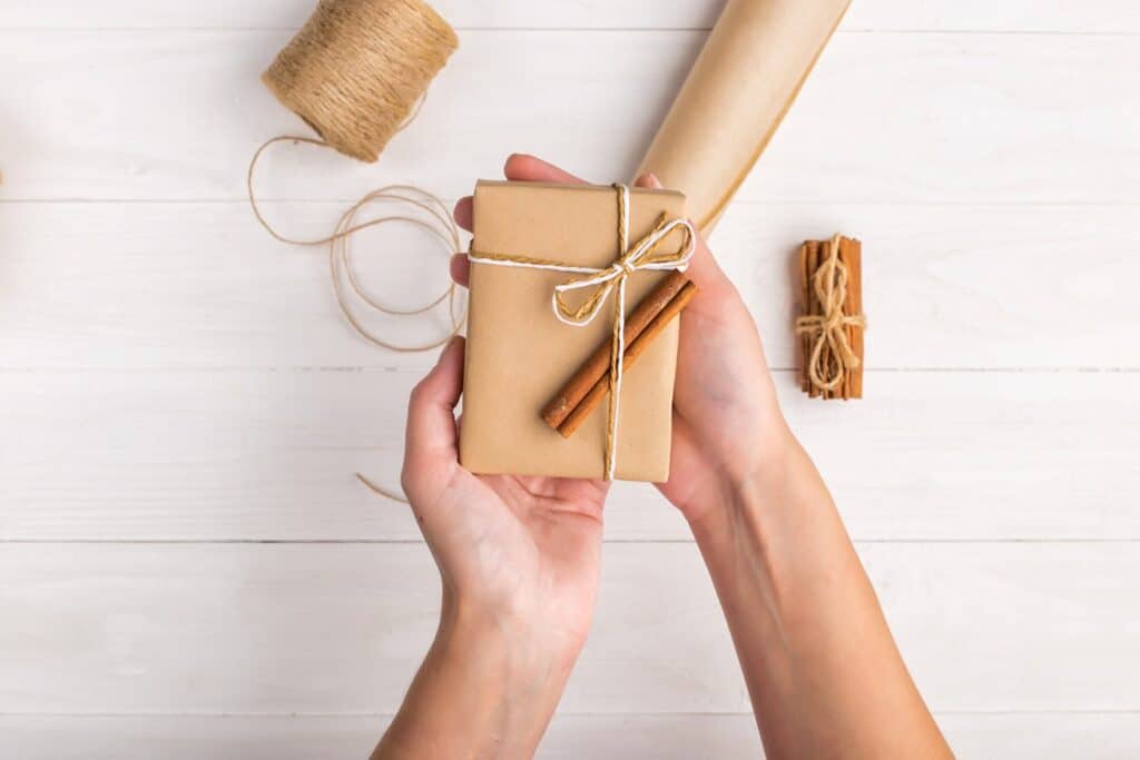 ידיים מחזיקות מתנה עטופה בנייר חום ברקע נייר עטיפה מספריים וחוט