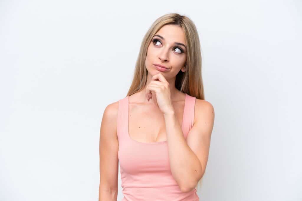 בחורה בגופייה ורודה חושבת יד על הסנטר רקע לבן