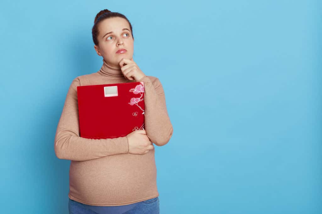 אישה בהריון מחזיקה מחברת אדומה וחושבת רקע תכלת