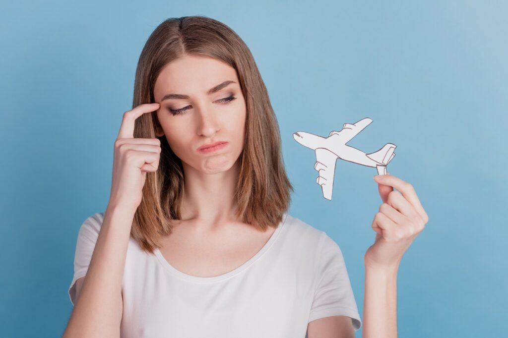 בחורה מחזיקה מטוס נייר וחושבת יד על הראש רקע תכלת